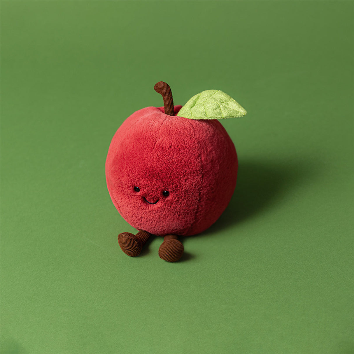 Plush toy shaped like a red apple with a green leaf on a green background