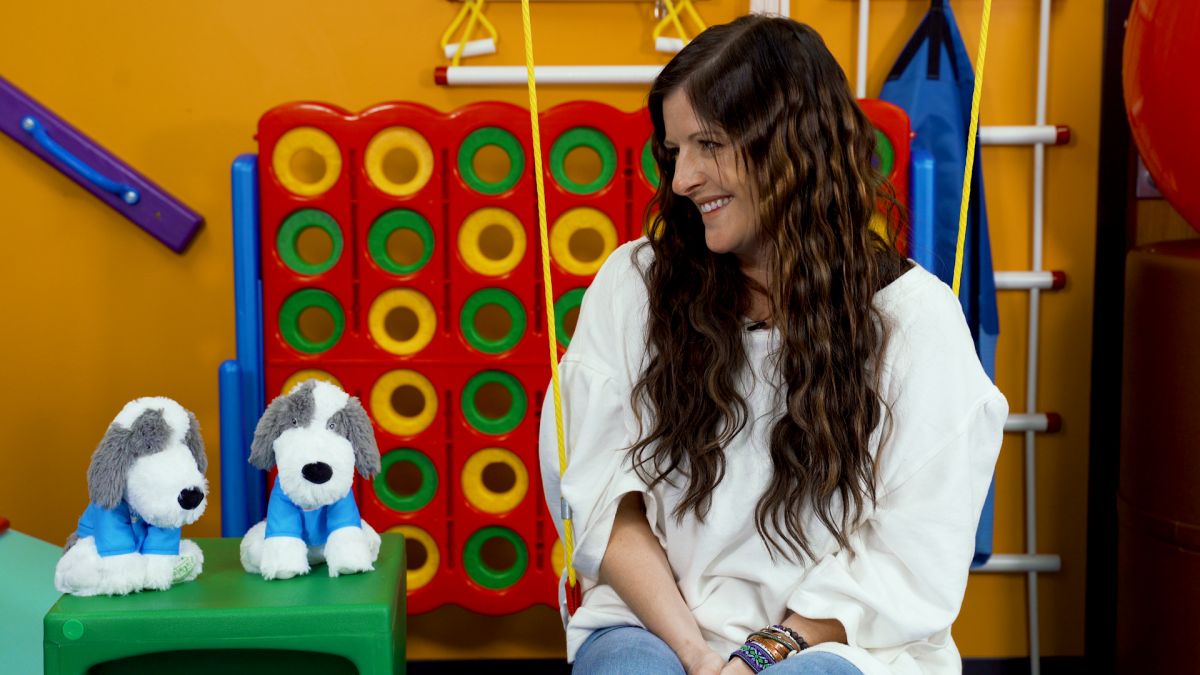 Gingerbread House Toys owner Kate Greene sits in a swing next to two stuffed animal dogs