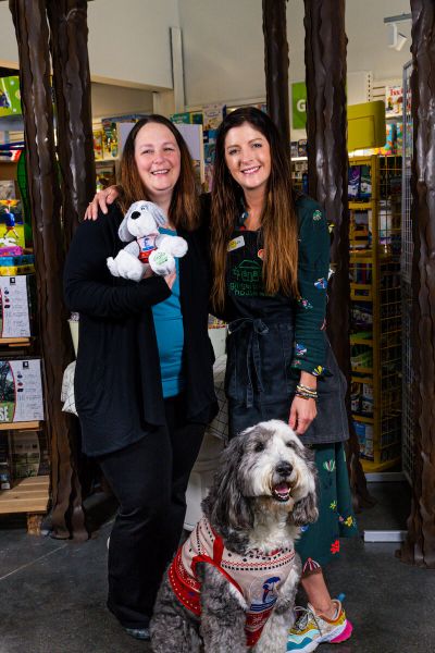 Two women embrace holding a stuffed animal replica of the real sheep dog sitting in front of them
